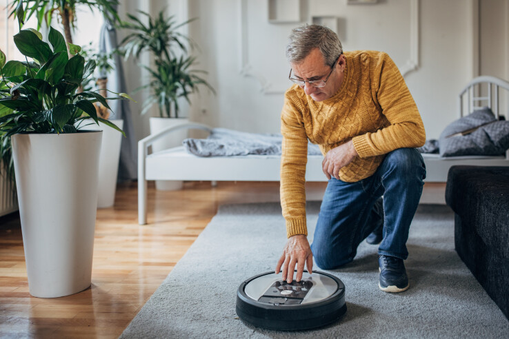 Un homme vérifie un robot aspirateur sur un tapis dans le salon avant de le mettre en marche.