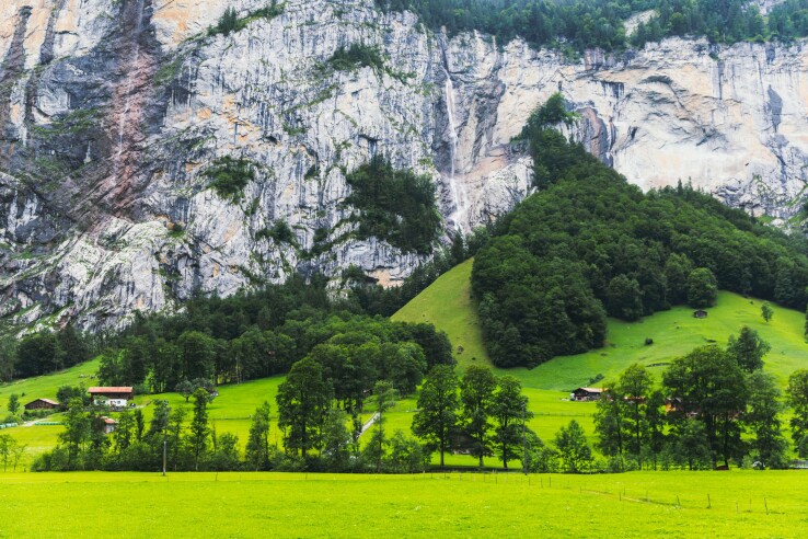 Une paroi rocheuse abrupte surplombant un paysage de montagne avec des maisons et des prairies : une zone typiquement exposée aux chutes de pierres dans les Alpes suisses.