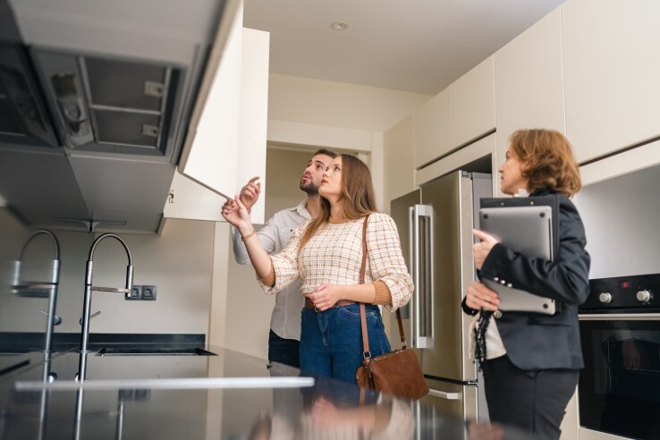 Des acheteurs potentiels visitent un appartement en copropriété en compagnie d'une agente immobilière et examinent l'équipement de la cuisine.