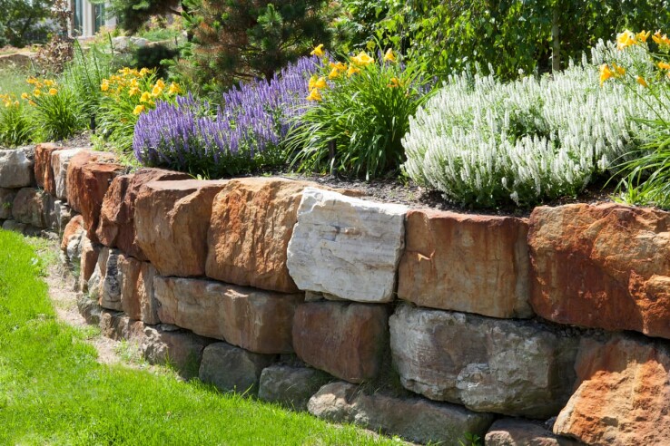 Mur de soutènement en pierre naturelle avec une plate-bande surélevée plantée, destiné à la stabilisation d'un talus dans le jardin.