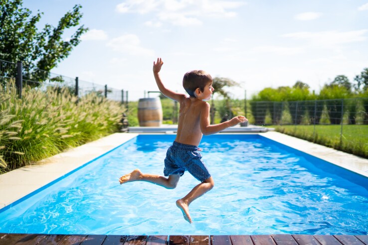 Un enfant plonge dans la piscine située dans le jardin d'une maison individuelle.