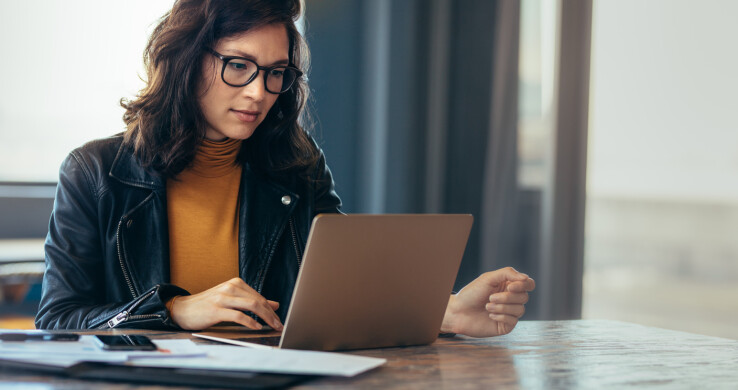 Une personne travaille sur son ordinateur portable et organise des documents pour la gestion d'une copropriété.