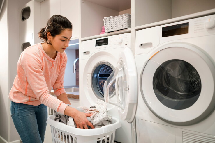 Une personne range le linge dans une machine à laver, dans une buanderie aménagée de façon moderne.
