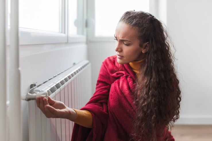 Une femme règle le thermostat d'un radiateur dans un appartement en location.
