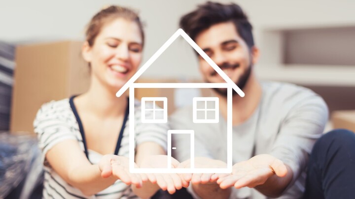 Un couple se réjouit d'avoir acheté sa propre maison et porte symboliquement sur ses mains le croquis d'une maison.