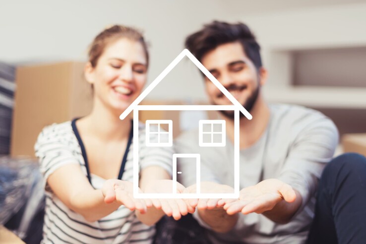 Un couple se réjouit d'avoir acheté sa propre maison et porte symboliquement sur ses mains le croquis d'une maison.